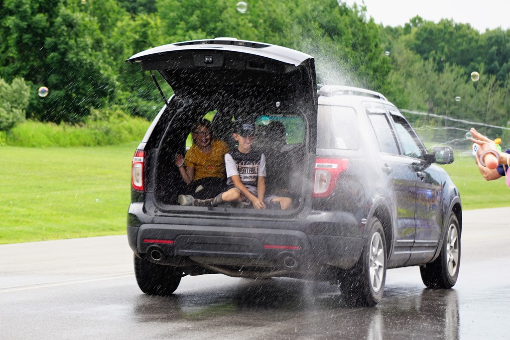 a van with the hatchback open and kids inside getting sprayed with water