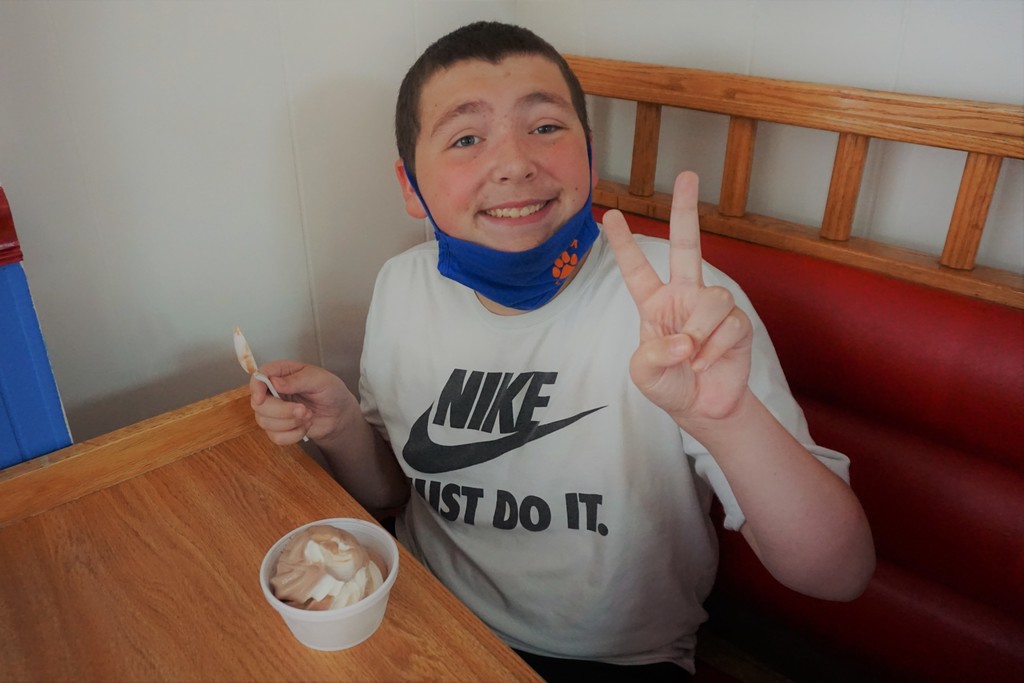 one smiling student holding up a peace sign with fingers and enjoying ice cream