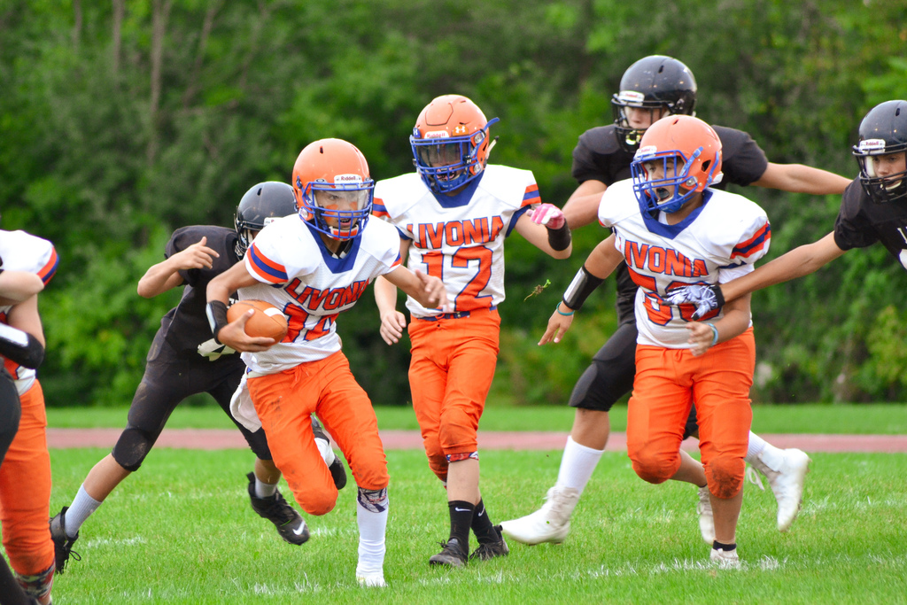 three football players running one holding ball
