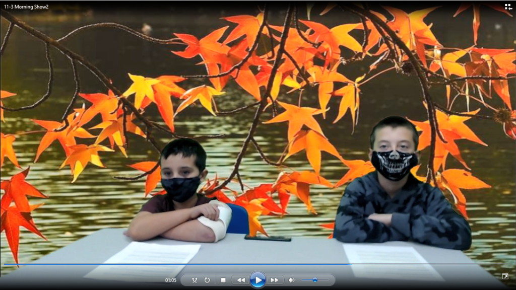 two students at news desk with leaves on the green screen