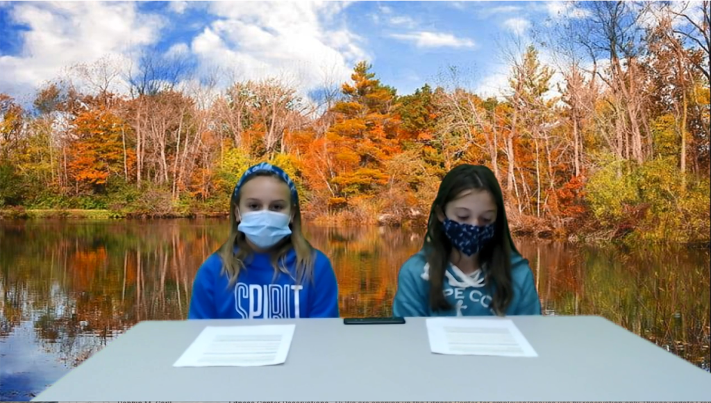 Screen shot of girls at desk with fall photo on green screen