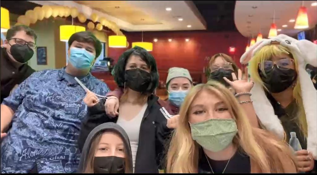 8 students with masks on with green screen of restaurant