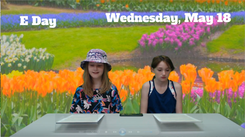 two students at news desk with tulips on green screen