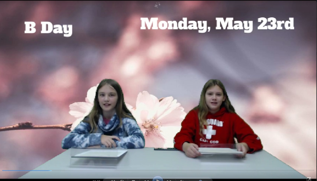 two students at news desk with flowers on green screen