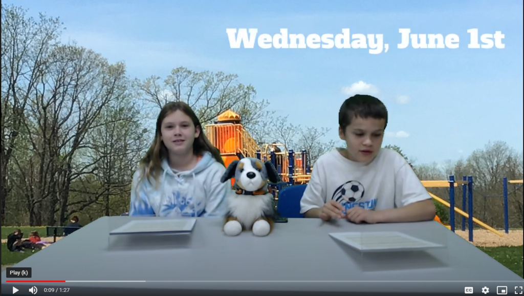 two students at news desk with ES playground on green screen with stuffed dog on desk
