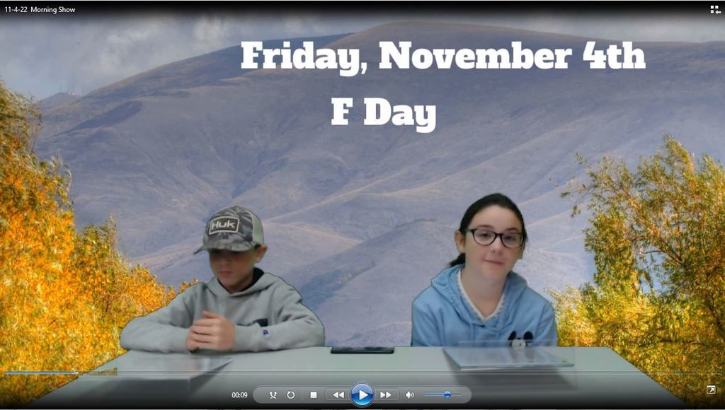 two students at news desk with fall hills on the green screen