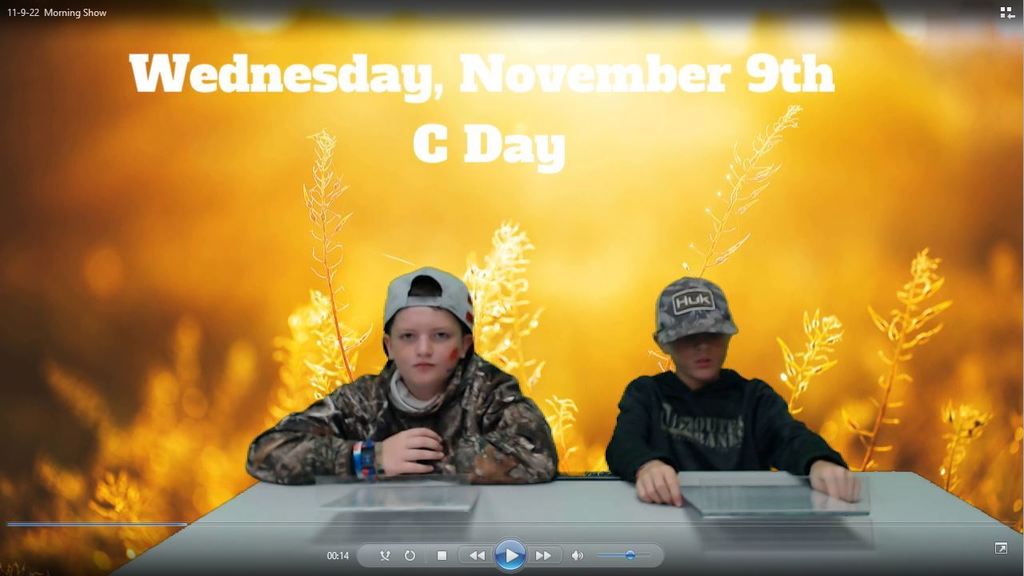 two students at news desk with golden field on green screen